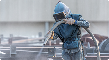 Person dressed in safety gear sandblasting a surface.