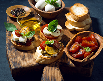 A wooden board with bread with cheese, tomato and leaves as toppings.
