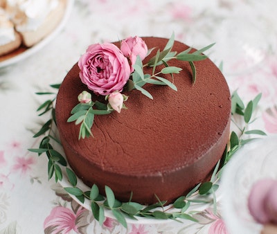 Chocolate cake with a pink flower on top of a white table.