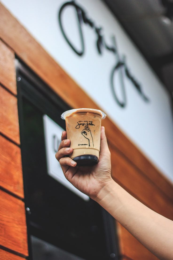 hand holding up a cup of iced coffee in front of a coffee shop