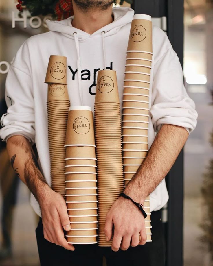 man in white hoodie holding stacks of paper cups